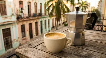 Una taza de café cubano con espuma dorada junto a una cafetera moka tradicional