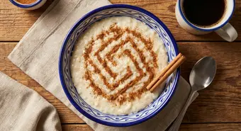 Bowl of Cuban arroz con leche rice pudding dusted with ground cinnamon and a cinnamon stick on the side.
