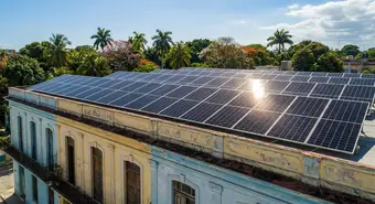 Solar panels installed on a building rooftop in Cuba with blue sky and tropical vegetation in the background