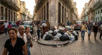 Accumulated garbage on a Havana street corner during the day, with concerned people walking by.