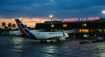 Avión de pasajeros estacionado en el aeropuerto de La Habana durante el atardecer con terminales oscuras al fondo.