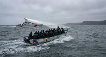 Cuban migrants in speedboat on rough waters near Cuban coast, with US Coast Guard vessel in background, dramatic scene