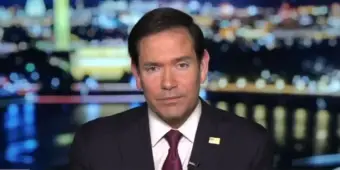 Marco Rubio speaking at a podium with flags.