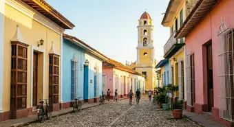 Calle empedrada colonial en Trinidad, Cuba, con casas de colores pastel y campanario del Convento de San Francisco al fondo